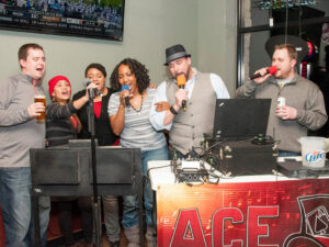 Group of diverse people singing karaoke at braskys using red microphones with ace your events