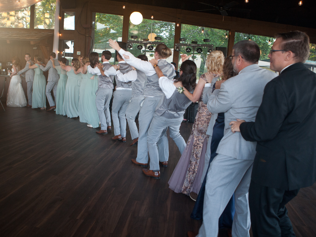 Wedding party conga line at wooded pavilion and dj in background